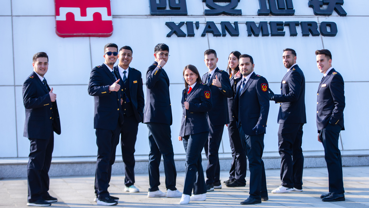 Foto de los jóvenes que están en China con su uniforme de trabajo, frente al nombre de Xi'an Metro