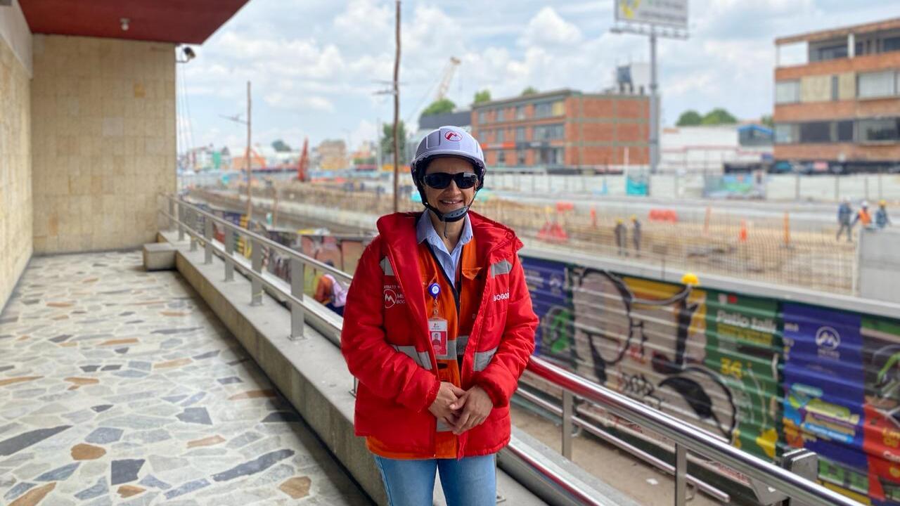 Foto desde la cintura de Amanda, con su uniforme de trabajo, sonriendo, de fondo la obra de la calle 72