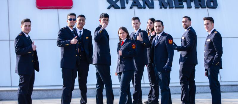 Foto de los jóvenes que están en China con su uniforme de trabajo, frente al nombre de Xi'an Metro